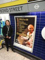 Maria Helena com cartaz no Metro de Londres, lembrando o Brasil.